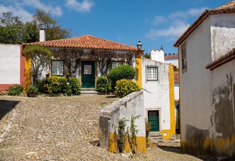 Rincones fotogénicos de Óbidos, una calle en pendiente y una casa con fachada de flores.