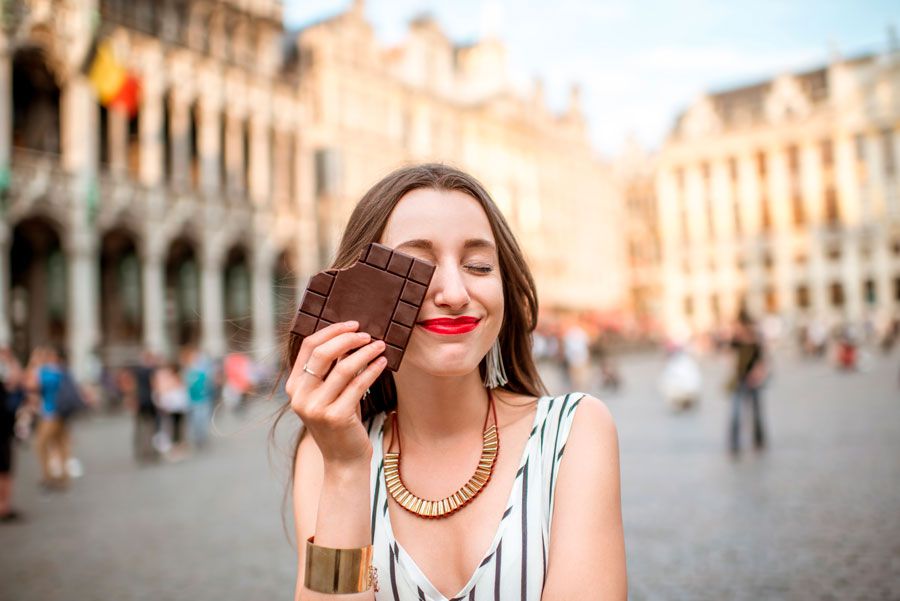 una mujer sonrie con una tableta de chocolate tapando la cara