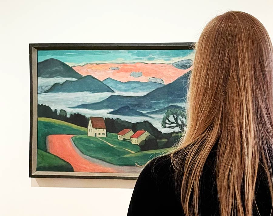 Una mujer mira un cuadro con  Los colores imaginarios de los paisajes de Gabriele Münter.
